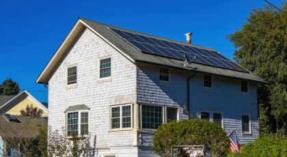 A modern two-story home with solar panels on its roof under a clear blue sky.