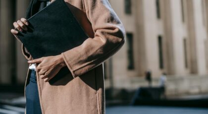A stylish woman in a coat holding a folder with a blurred building background, embodying professional elegance.