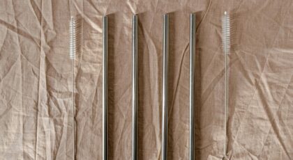 Set of stainless steel straws with cleaning brushes on a textured brown background.