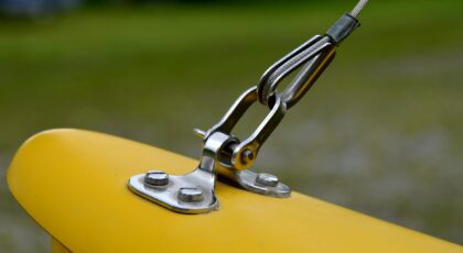 Detailed view of a metal wire rope fastened to a bright yellow surface outdoors.