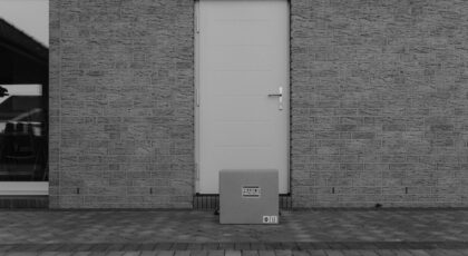 A grayscale photo of a package placed in front of a closed door on a concrete porch.
