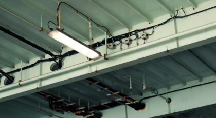Detailed view of industrial ceiling light and wiring at a low angle in an indoor setting.