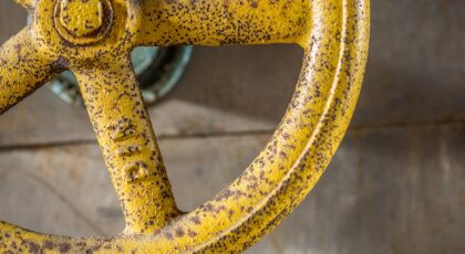 Close-up of a rusty yellow valve wheel in an industrial environment, showcasing texture and color contrast.