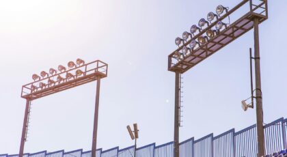 Bright stadium spotlights under a clear blue sky by empty seats, symbolizing sports events.