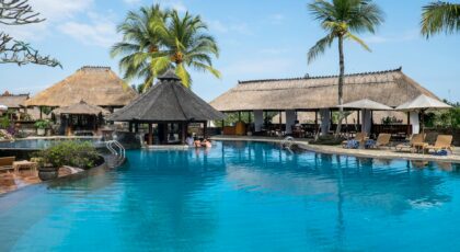 Relax by the tropical pool at a luxurious resort in Bali, featuring palm trees and serene blue waters.