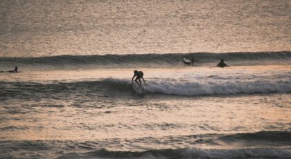 A surfer rides the waves during a stunning sunset on a Bali beach, showcasing water sports excitement.