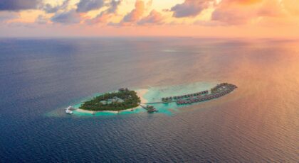 A picturesque aerial view of a tropical island resort surrounded by clear blue ocean during a vibrant sunset.