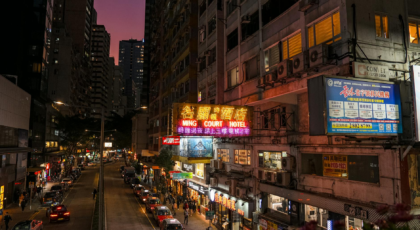 Bustling city street at dusk with colorful neon signs and urban architecture.