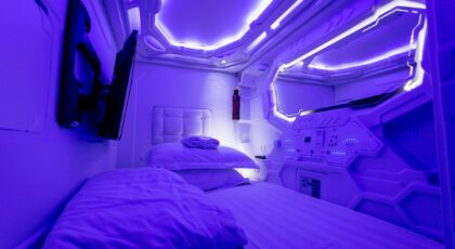 Explore a futuristic capsule hotel room adorned with calming ultraviolet lighting, perfect for a tranquil stay.