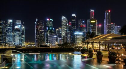 Vibrant night view of Singapore's illuminated skyline with a foreground infinity pool reflecting city lights.