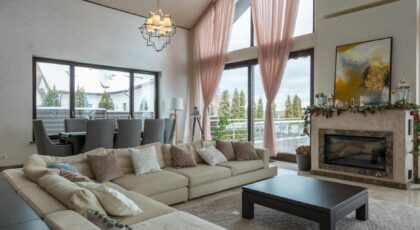 Comfortable lounge zone with soft furniture against fireplace near huge windows in villa