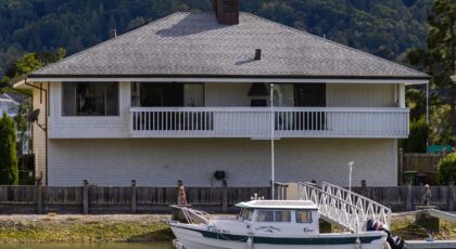 A serene waterfront house with a docked boat in a lush, forested area.