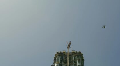 A bird soars above a building under construction set against a clear blue sky.