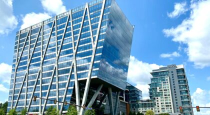 Tall modern office building with glass facade in an urban setting under a clear blue sky.