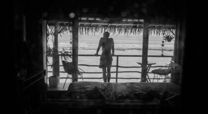 A person gazing at the tranquil ocean from a tropical resort room balcony.