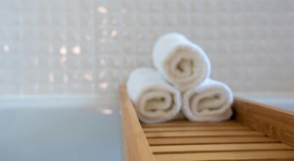 A close-up of rolled white towels on a wooden bath tray in a modern bathroom.