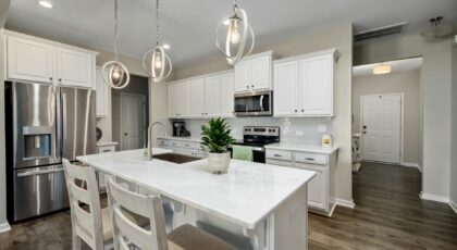 A spacious and modern kitchen with white cabinets and elegant hanging lights.