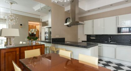 Stylish kitchen furnished with glossy cupboards and dining table with modern appliance including hood with built in stove and microwave