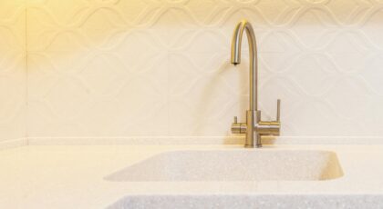 Sink under stainless steel tap against decorative wall illuminated by light in contemporary house kitchen