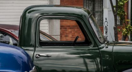 Close-up of a classic green GMC truck parked on a street in an urban setting.