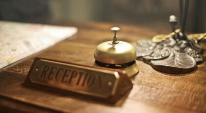 Old fashioned golden service bell and reception sign placed on wooden counter of hotel with retro interior