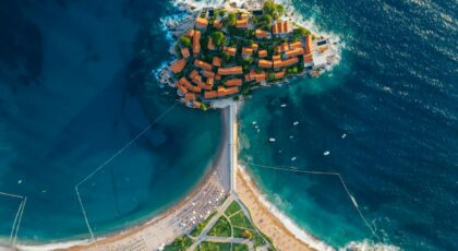 Stunning aerial photo of a coastal island with turquoise waters and vibrant roofed buildings.