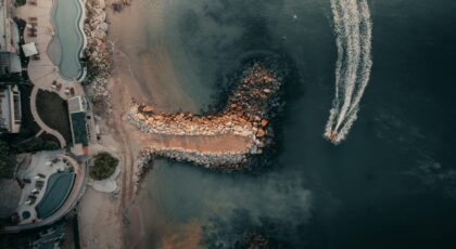 Aerial drone view of a resort by the ocean with a rocky coastline and boat in Puerto Vallarta, Mexico.
