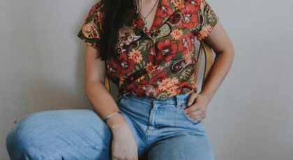 Stylish woman wearing a vibrant floral shirt and denim jeans, casually sitting indoors.