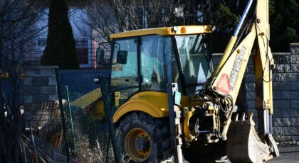 A yellow excavator rests on an urban construction site during daylight.