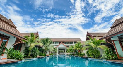 Spacious swimming pool surrounded by tropical villas under a bright blue sky, perfect for relaxation.