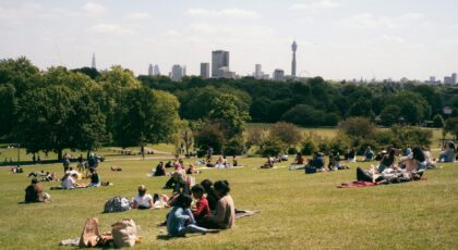 People relaxing on Primrose Hill with a view of the London skyline on a sunny day.