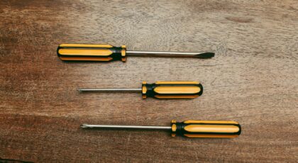 Flat lay of three screwdrivers on a wooden table, showcasing different types.
