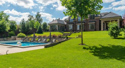 Spacious elegant mansion with a pristine pool, lush garden, and clear blue sky.