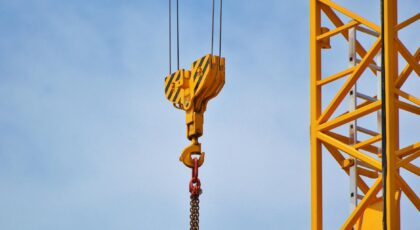 Close-up of a yellow crane arm against a clear blue sky, showcasing industrial equipment.