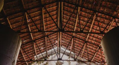 View of architectural wooden roof trusses inside an old factory with exposed ceiling and natural light.