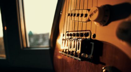 Ambient close-up of an electric guitar's bridge illuminated by sunset light through a window.