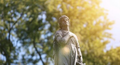 A stone statue is beautifully backlit by the sun with lush greenery as a backdrop.