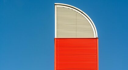 Abstract view of a red and gray metal architectural structure against a clear blue sky.