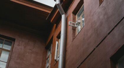 A brown building exterior with pipes and windows, photographed from a low angle.