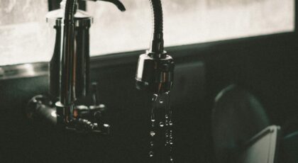 Close-up of a kitchen faucet with water droplets falling into the sink, captured in a minimalist style.