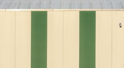 A minimalist industrial building facade featuring vertical green stripes and metal roof.