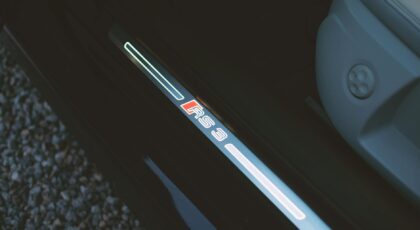 Detailed view of Audi RS3 door sill featuring illuminated logo, captured in moody lighting.
