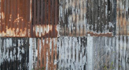 A close-up of a rusty corrugated metal wall with peeling paint, showcasing decay.