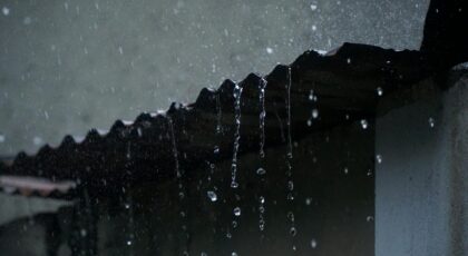 Close-up of rainwater flowing off a corrugated roof in low light, creating a serene ambiance.