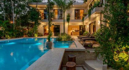 Modern luxury villa with a lit pool and tropical garden. Evening view.