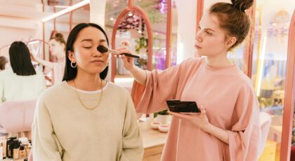 Asian woman receiving makeup from artist in bright, modern beauty salon.