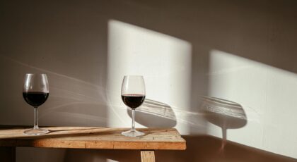 Two glasses of red wine on a wooden table with dramatic shadows and reflections.