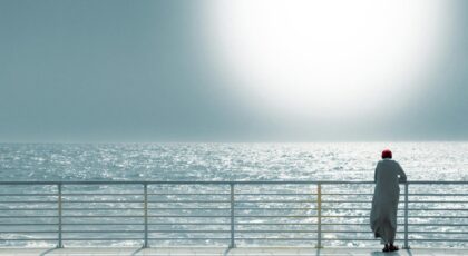A contemplative scene of a person in traditional attire gazing at the sunlit ocean horizon.