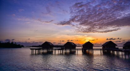 Serene view of overwater villas silhouetted against a colorful sunset by the sea.