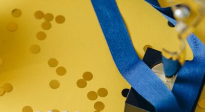 Gold medal and winner's trophy on a vibrant yellow confetti background, symbolizing success and victory.